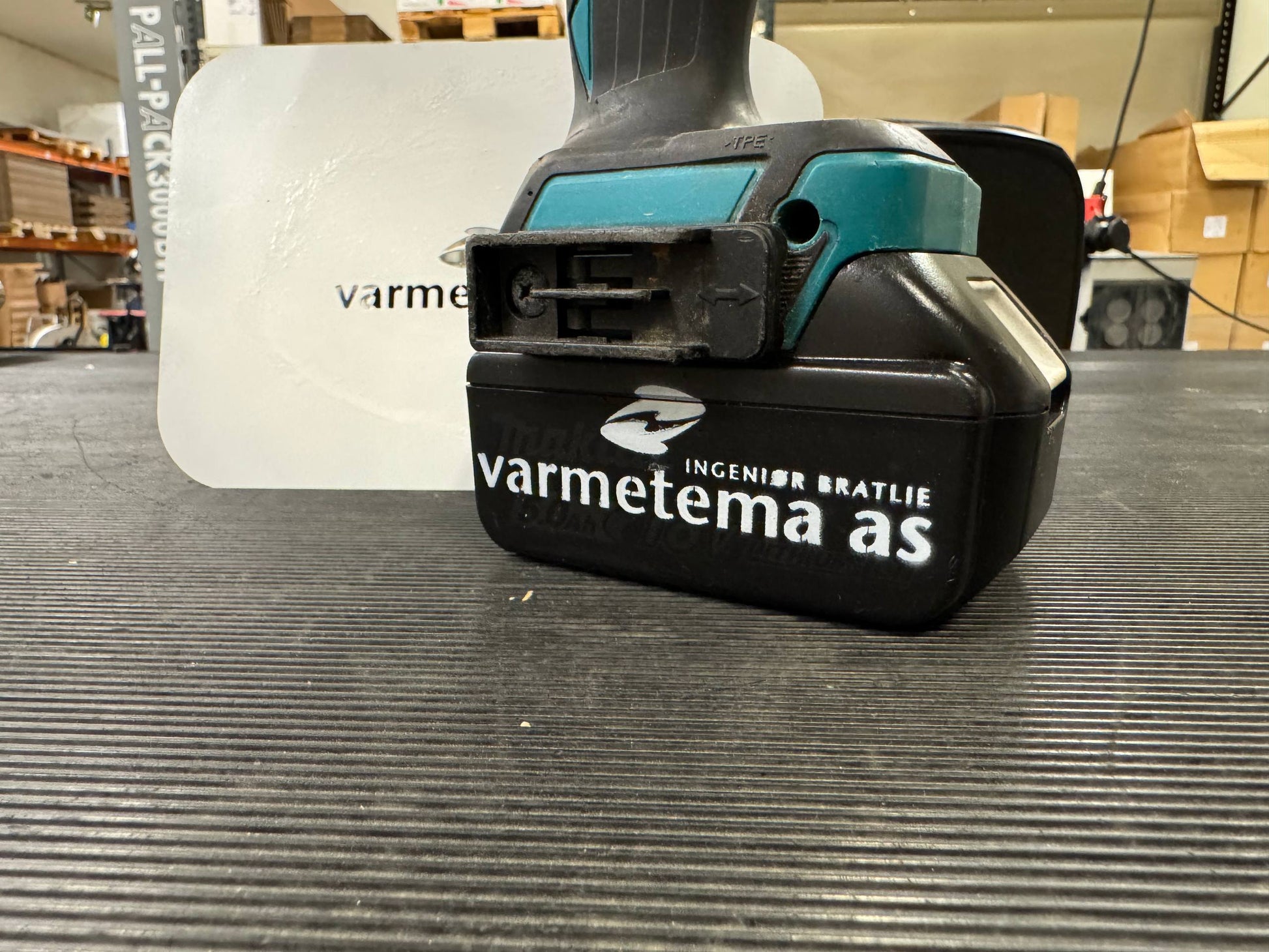 Makita-verktøybatteri merket Varmetema med sjablong i bakgrunnen